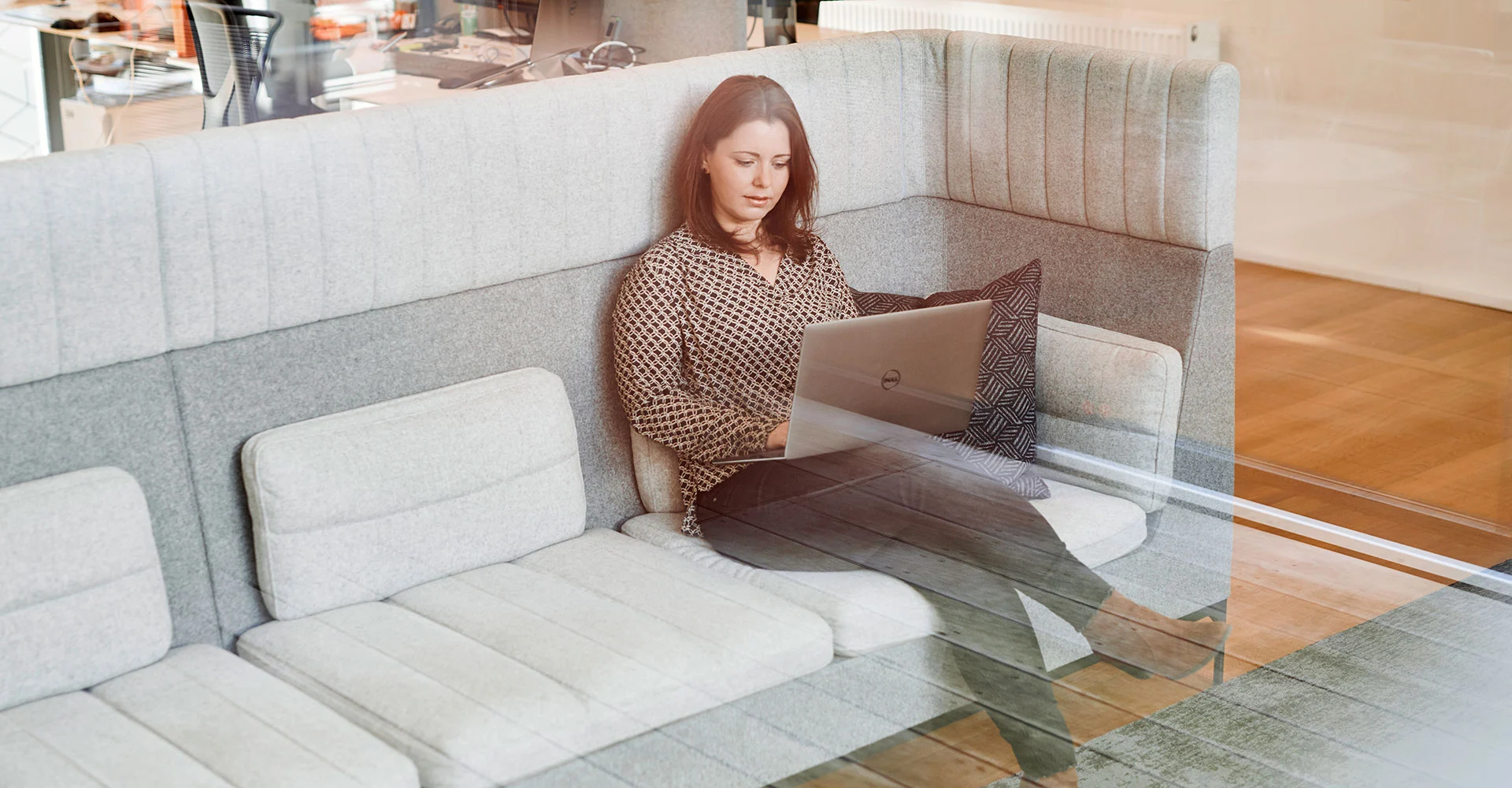 Mitarbeiterin sitzt auf einem Sofa im Büro und arbeitet am Laptop