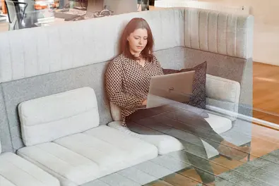 Mitarbeiterin sitzt auf einem Sofa im Büro und arbeitet am Laptop