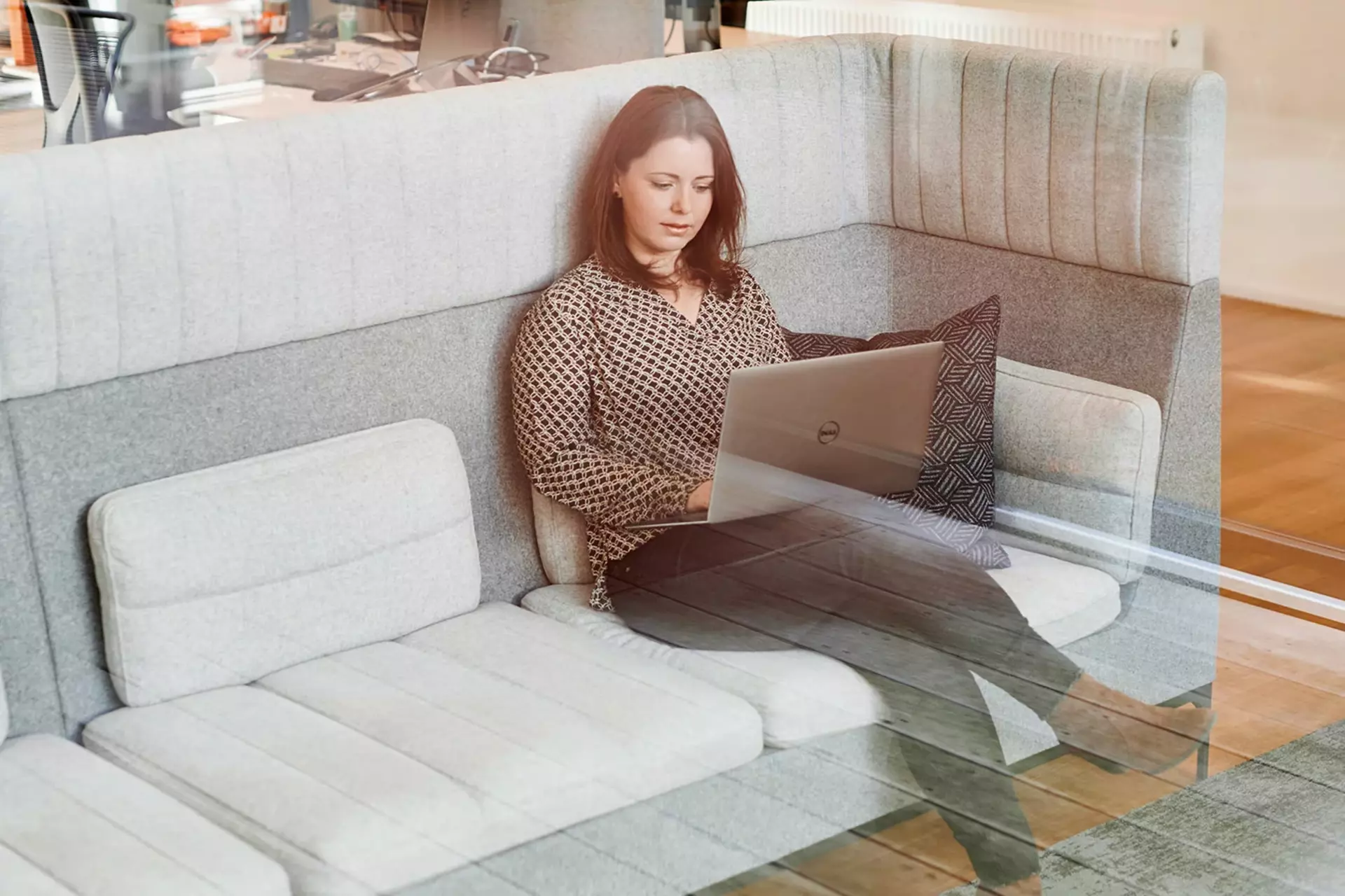 Mitarbeiterin sitzt auf einem Sofa im Büro und arbeitet am Laptop