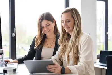 Zwei Mitarbeiterinnen tauschen sich am Arbeitsplatz aus