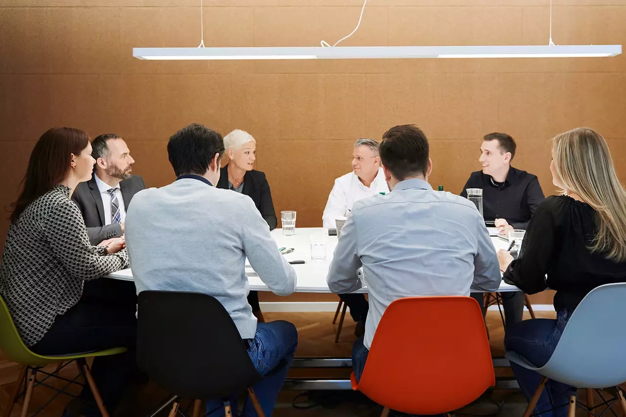 Meeting Acht Mitarbeitende sitzen im Meetingraum gemeinsam an einem Tisch