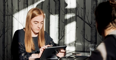 Mitarbeiterin sitzt mit einem Tablet im Pausenraum
