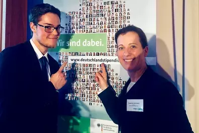 Deutschlandstipendium 2018/2019 Zwei Personen die vor dem Plakat der Veranstaltung des Deutschlandstipendiums stehen