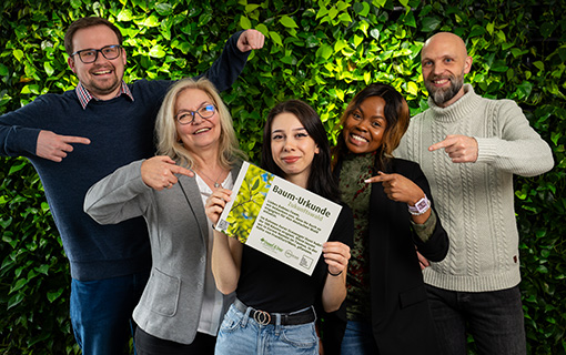 Babtec-Teammitglieder mit der „Baum-Urkunde Zukunftswald“ vor einem blättrig-grünen Hintergrund. 